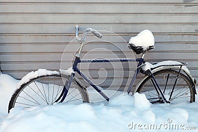 old bicycle under the snow on the background of a metal wall Stock Photo