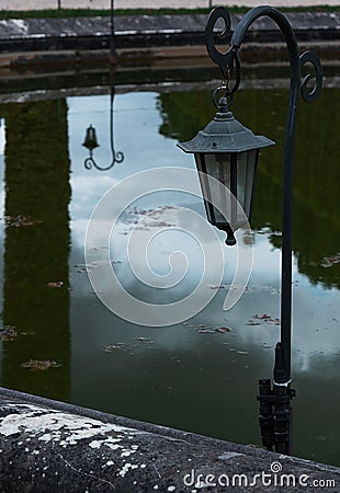 Old black iron street lantern in the park against the background of reflections in the water Stock Photo