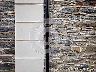 Old black painted iron guttering pipe joined to a stone wall Stock Photo