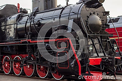 Old black and red retro steam locomotive at the railway station. Vintage train staying on the railroad. Stock Photo