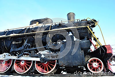 Old black train with red elements covered with snow, standing on platform against blue sky background, side of locomotive Stock Photo