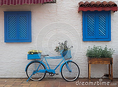 Old blue bicycle stands on the street near the wall with windows with wooden shutters Stock Photo