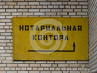 Old yellow board of the closed notarial office in Russia with arrow indicating the entrance. Brick wall in background. Stock Photo