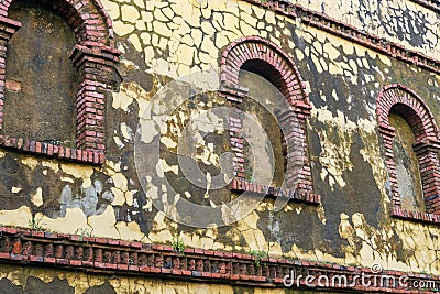 Old brick arched windows against the cracked mossy yellow wall Stock Photo