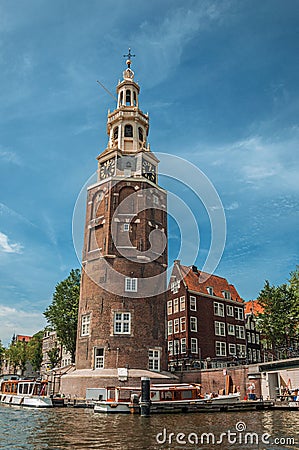 Old brick bell tower and buildings near the tree-lined canal with moored boats and blue sky in Amsterdam. Stock Photo