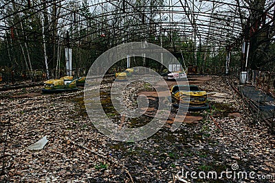 Old broken rusty metal radioactive yellow cars, children`s electric cars, abandoned among vegetation, the park of culture and rec Editorial Stock Photo
