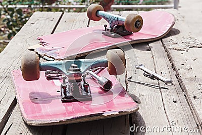 The old broken skateboard lies with a spanner on a wooden table in the open air Stock Photo
