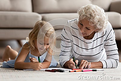 Old grandma little grandkid drawing pictures lying on warm floor Stock Photo