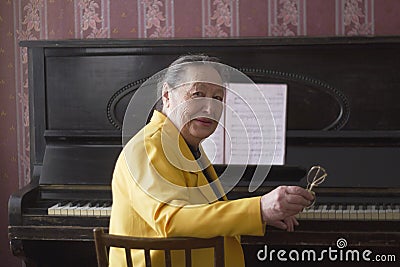 Old charming lady pianist in the yellow jacket seating at the piano Stock Photo