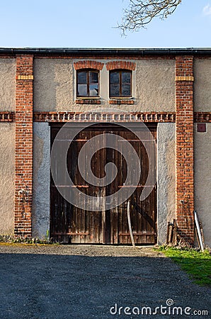 Old closed rustig barn gates in red brick wall. Rural door in sunset light. Stock Photo