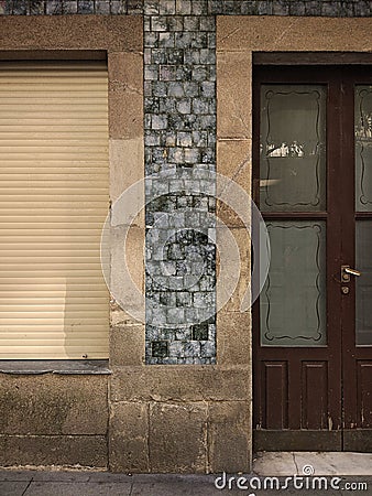 Old closed window with wooden shutter and a door with translucent glass in a granite stone wall and blue tiles Stock Photo