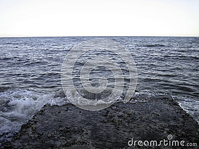 The old concrete breakwater is slightly washed by weak waves on the seashore Stock Photo