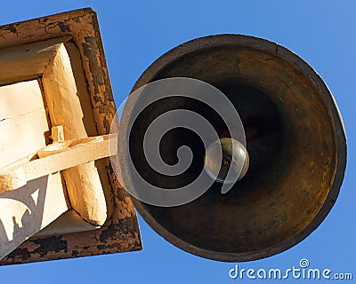 Old copper bell on a wooden pillar bottom view, signal bell. Outdated device for warning and gathering people, alarm. Beautiful Stock Photo