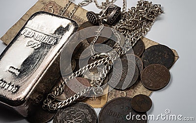 The old copper and silver coins, silver bullion, and jewelry lay on old bills. Stock Photo