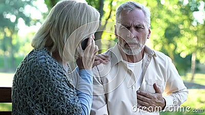 Old couple sitting on bench, man suffering arrhythmia, wife calling emergency Stock Photo