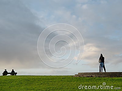 Old couple sitting on a bench in a park, Young couple standing very close to each other. Concept old and young, Difference in Editorial Stock Photo