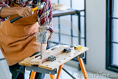 Old craftsman use hammer and chisel to work with wood and produce some product in his workplace during day time Stock Photo