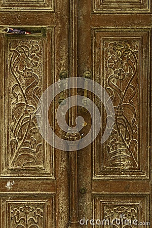 Old damaged decorated faded brown historic wooden door with handles and newspaper slot from Sicily Stock Photo
