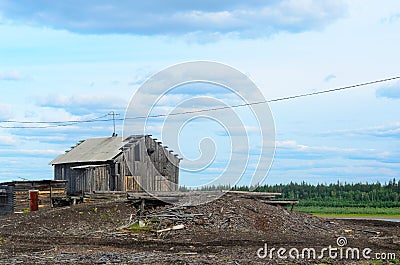 Old deserted barn with a house standing on the background of a pile of abandoned logs on a derelict sawmill. Stock Photo