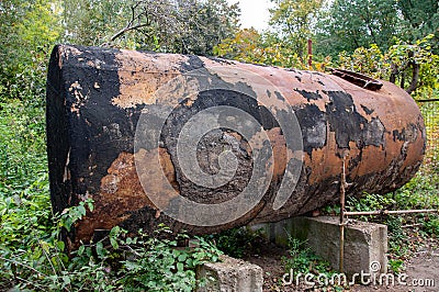 Old dilapidated water tank coated with stains of shabby black paint Stock Photo