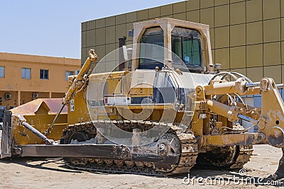 Old dirty extremely heavy bulldozer arrived to repair station. Yellow earthmover dozer machine. Stock Photo