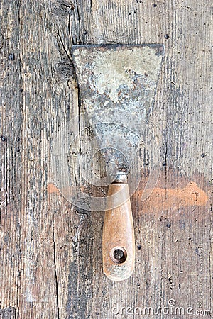 Old, dirty putty knife against wooden plank. Stock Photo