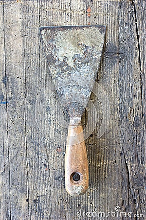 Old, dirty putty knife against wooden plank. Stock Photo