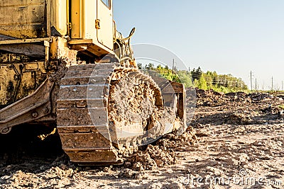 Old dirty yellow crawler bulldozer, rear view, the construction machine is lit by the rays of the setting sun Stock Photo