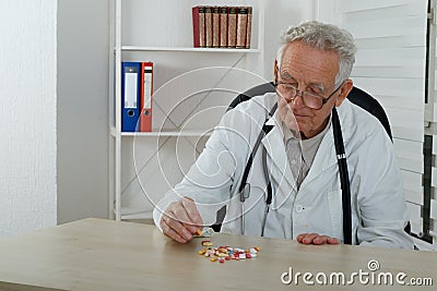 Old doctor observe colorfully pills in consulting room Stock Photo