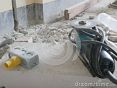 Old dusty angle grinder, with a diamond cutting disc, and an electrical back box placed on a lightweight concrete block Stock Photo