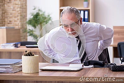 Old male employee suffering from radiculitis at workplace Stock Photo