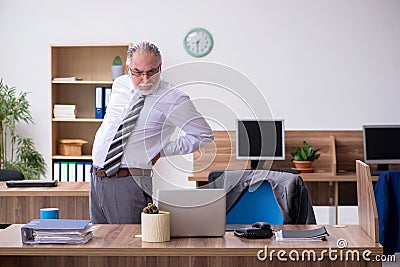 Old male employee suffering from radiculitis at workplace Stock Photo