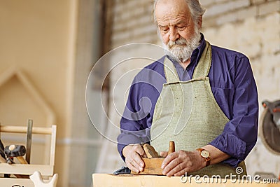 Old experienced carpenter working with wooden planer on plank workshop. Stock Photo