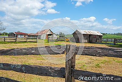 Old farm sheds beyond post and rail fences in rustic rural scene Stock Photo