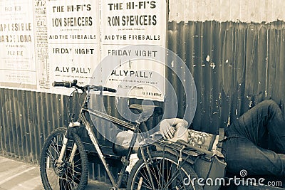 Old-fashioned posters for show at the Ally Pally on corrugated iron wall above a man asleep Editorial Stock Photo