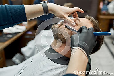 Old fashioned shaving. Barber shaving young handsome bearded man with dangerous straight razor. Working in barbershop Stock Photo