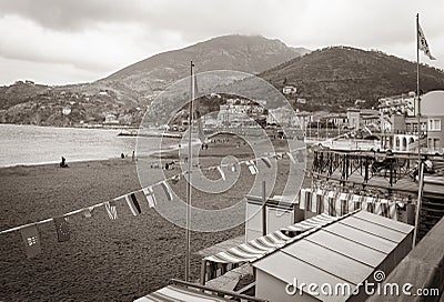 Old-fashioned style faded image at beach of Riomaggiore with beach-side buildings, flags and surrounding hills Editorial Stock Photo