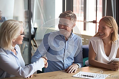 Old female broker handshake happy young couple clients make deal Stock Photo