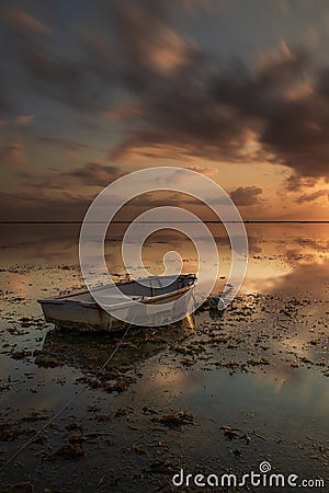 Old fisherman boat. Seascape. Fishing boat at the beach during sunrise. Low tide. Water reflection. Cloudy sky. Slow shutter speed Stock Photo