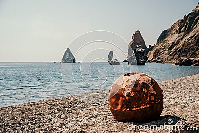 Old rusty round floating marine mines on the beach with rocky shore and sea background. Pollution, nature protection Stock Photo