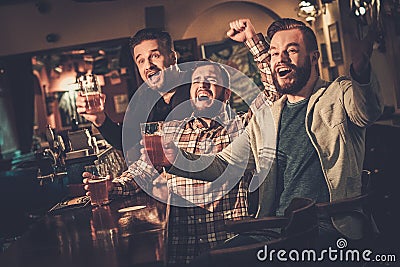 Old friends having fun watching a football game on TV and drinking draft beer at bar counter in pub. Stock Photo