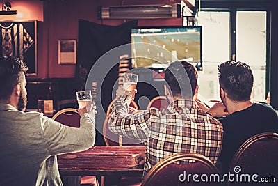 Old friends having fun watching a football game on TV and drinking draft beer at bar counter in pub. Stock Photo