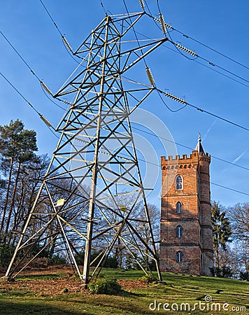 Old gothic tower sits behind modern electricity pylon Stock Photo