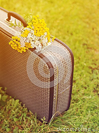 Old gray suitcase and bouquet of yellow wild flowers on a green grass in summer sunny day. Stock Photo