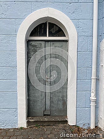old grey door with a white arched frame in a brick wall painted in blue Stock Photo