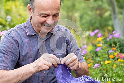 Old handsome man sitting at his summer garden with the knitting needles. Stock Photo