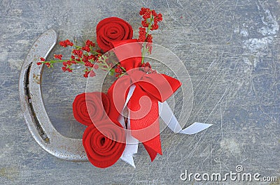 An old horseshoe decorated with red roses made of felt with red and white ribbons on a worn and scratched steel background. Stock Photo