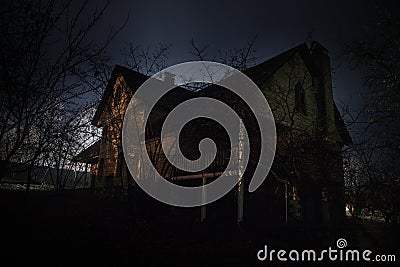 Old house with a Ghost in the forest at night or Abandoned Haunted Horror House in fog. Old mystic building in dead tree forest. Stock Photo