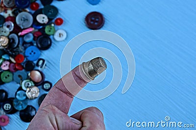 Iron thimble on finger against the background of colored buttons on the table Stock Photo