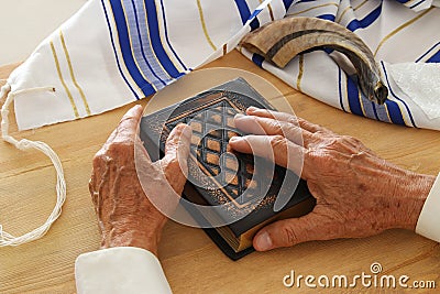 Old Jewish man hands holding a Prayer book, praying, next to tallit and shofar horn. Jewish traditional symbols. Rosh hashanah Stock Photo